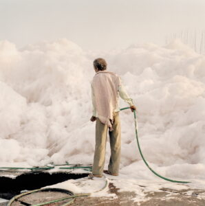 A worker with a water hose tries to tame an iceberg of foam created by the chemical waste dumped by the factories along the Yamuna river, Delhi, 2015