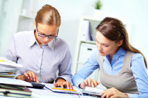 Portrait of two young businesswomen working with calculators in office
