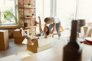 Young couple moved to a new house or apartment. Having fun with cardboard boxes, relaxing after cleaning and unpacking at moved day. Look happy. Family, moving, relations, first home concept.