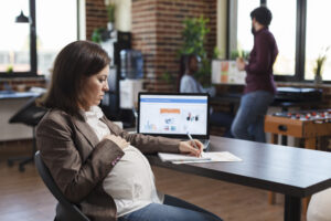 Pregnant woman analyzing economic growth of company and reviews financial and management chart. Finance agency employee reviewing project development while looking at chart on monitor.